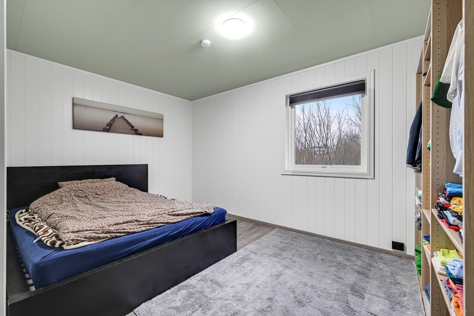 Romslig hovedsoverom med laminat på gulv, panel på veggene og malte takplater. Galleribilde