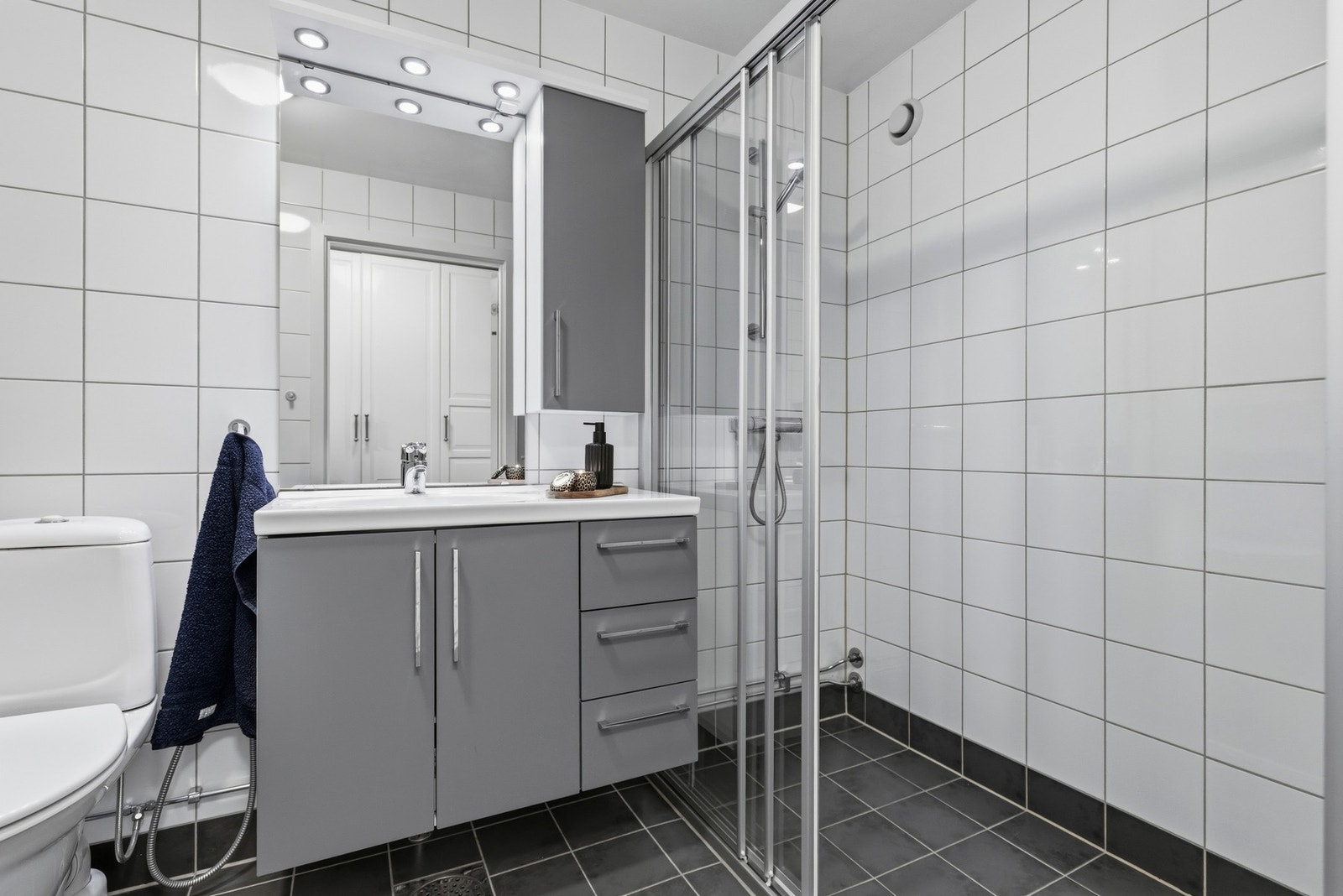 Veggmontert servantinnredning med heldekkende vask og ett-greps armatur i krom. Avtrekket på badet er tilkoblet felles mekanisk avtrekk. Galleribilde