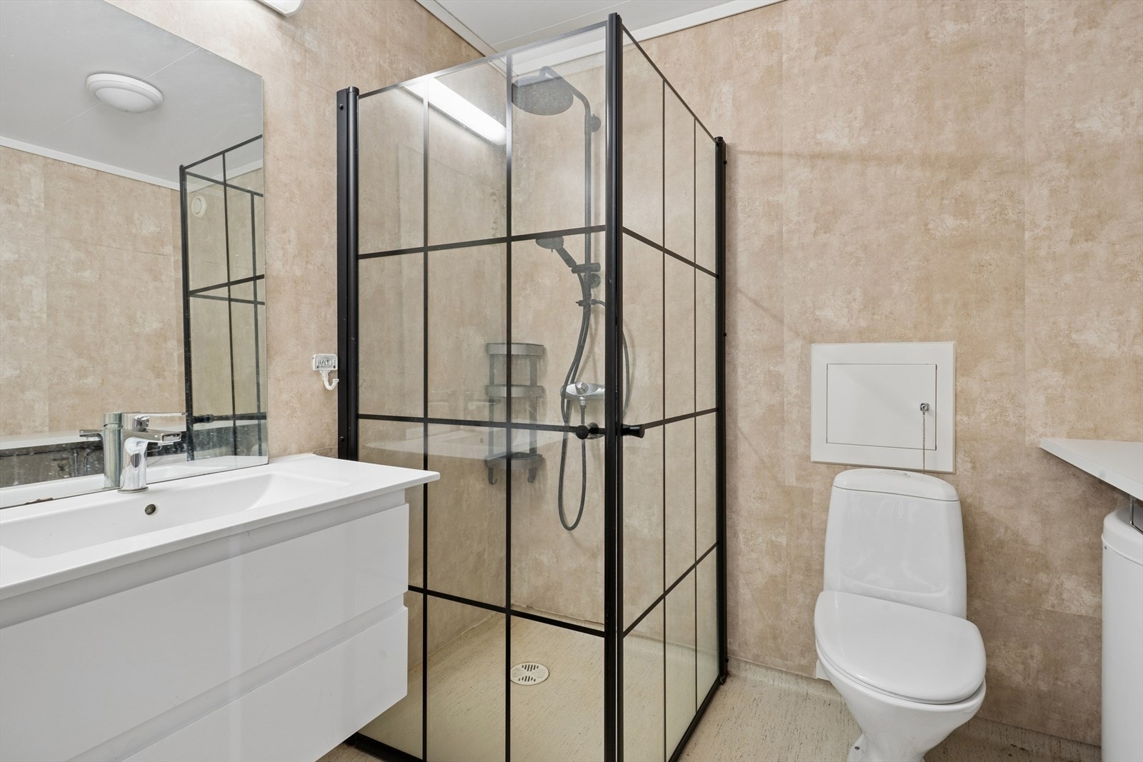 Innredningen består av servantinnredning, gulvstående toalett og dusjhjørne med innfellbare glassvegger. Det er også opplegg for vaskemaskin. Galleribilde