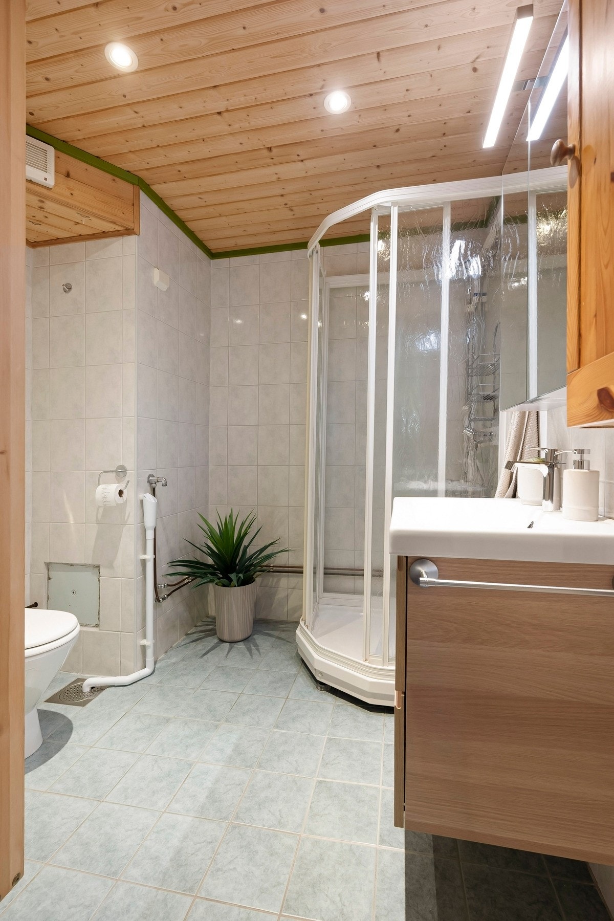 Badet inneholder servantseksjon med skuffer, dusjkabinett, gulvmontert toalett og opplegg for vaskemaskin Galleribilde