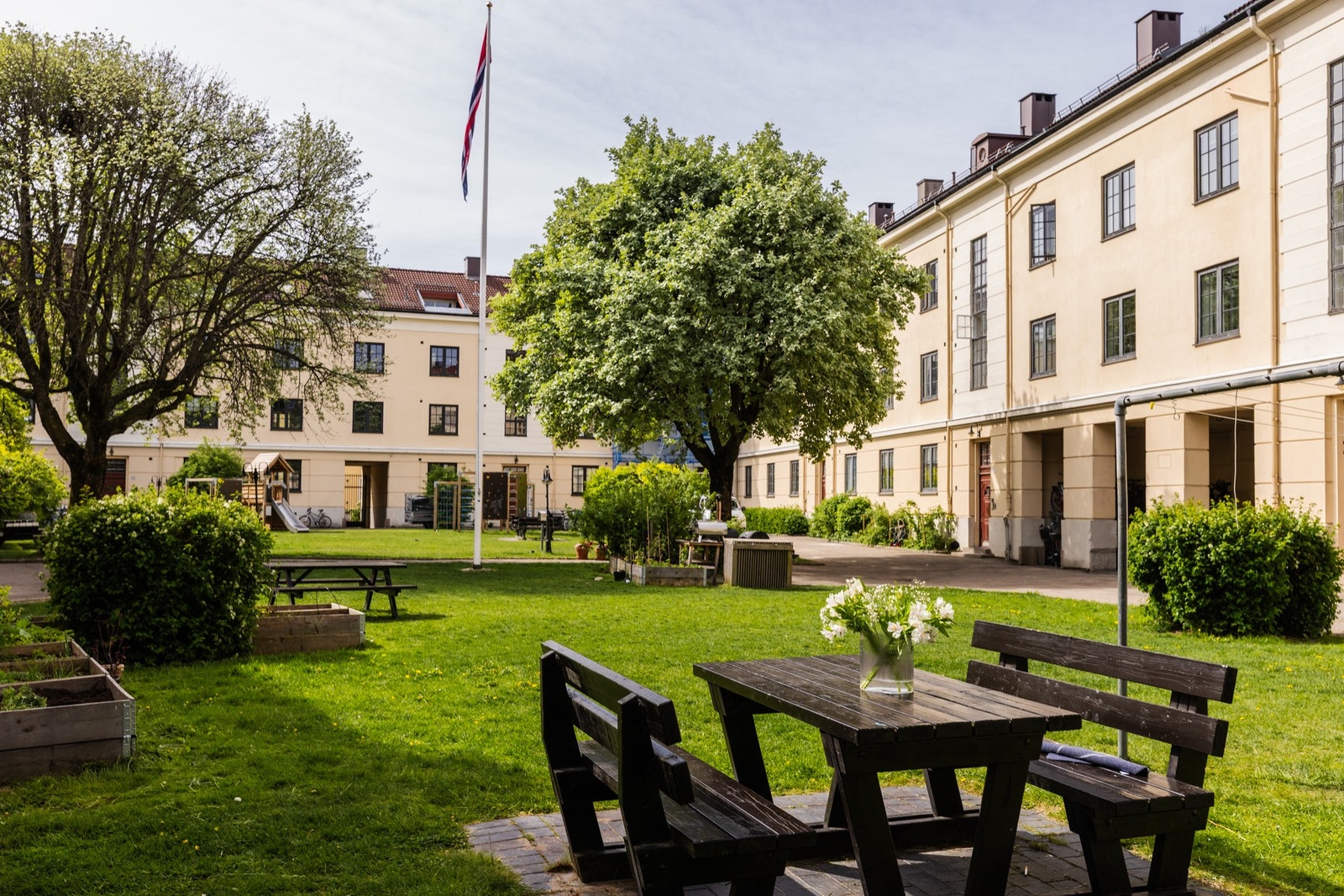 Nydelig gårdsrom i engelsk hageby-stil med lekeområder, sittegrupper, frodig beplanting og sosiale soner. Galleribilde