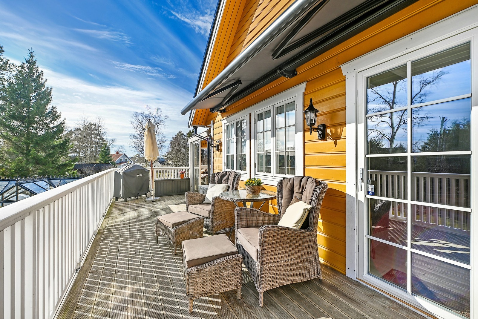 Romslig terrasse med markise og rekkverk, tilknyttet en gulmalt bolig. Galleribilde