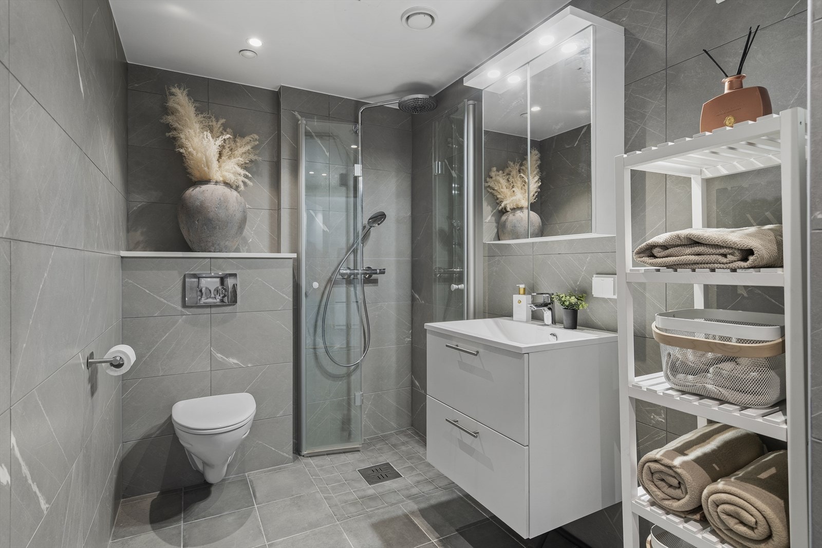 Badet er lekkert innredet med store, grå fliser på gulv og vegger. I gulvet har man også varmekabler for ekstra komfort. Galleribilde
