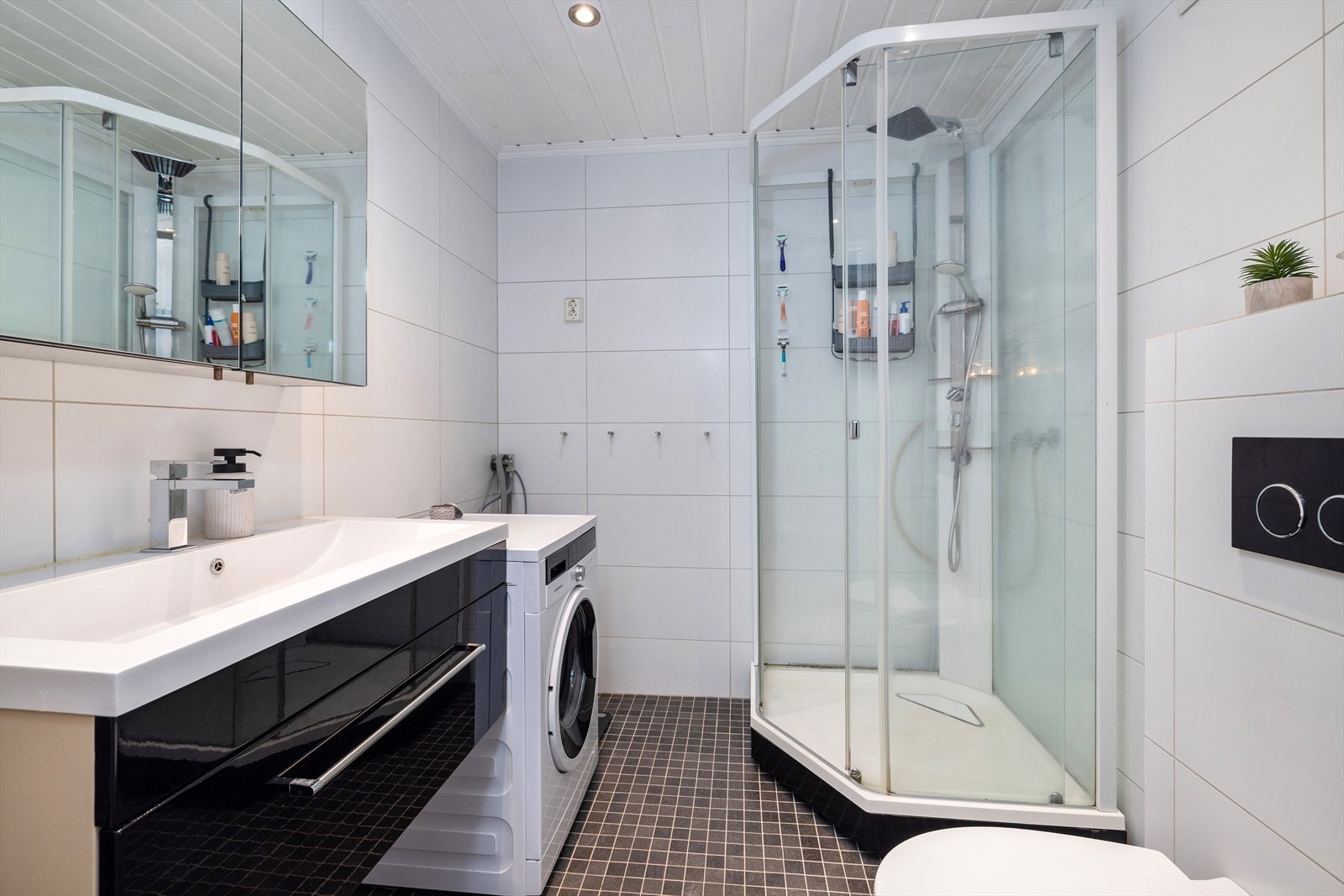 Badet i 1.etasje er flislagt med varmekabler i gulv. Badet er innredet med baderomsinnredning, speilskap, vegghengt toalett og dusjkabinett. Rommet har opplegg for vaskemaskin. Galleribilde