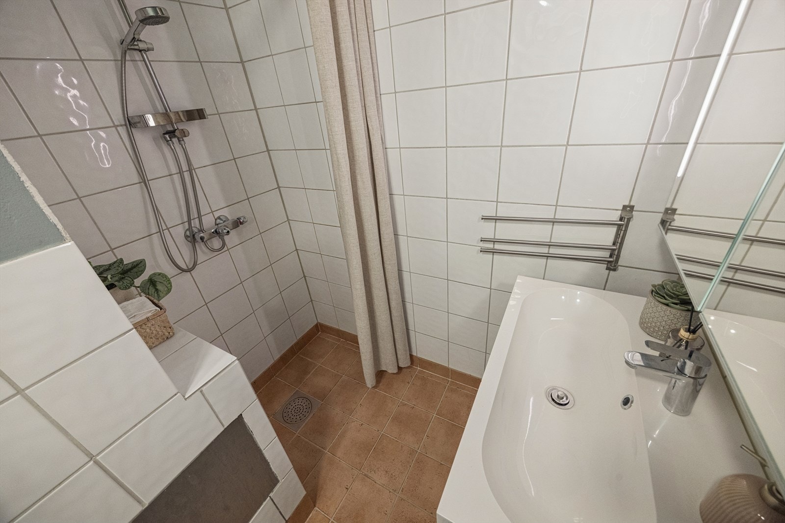 Badet har flislagte overflater, servantinnredning og en praktisk dusjnisje. Galleribilde