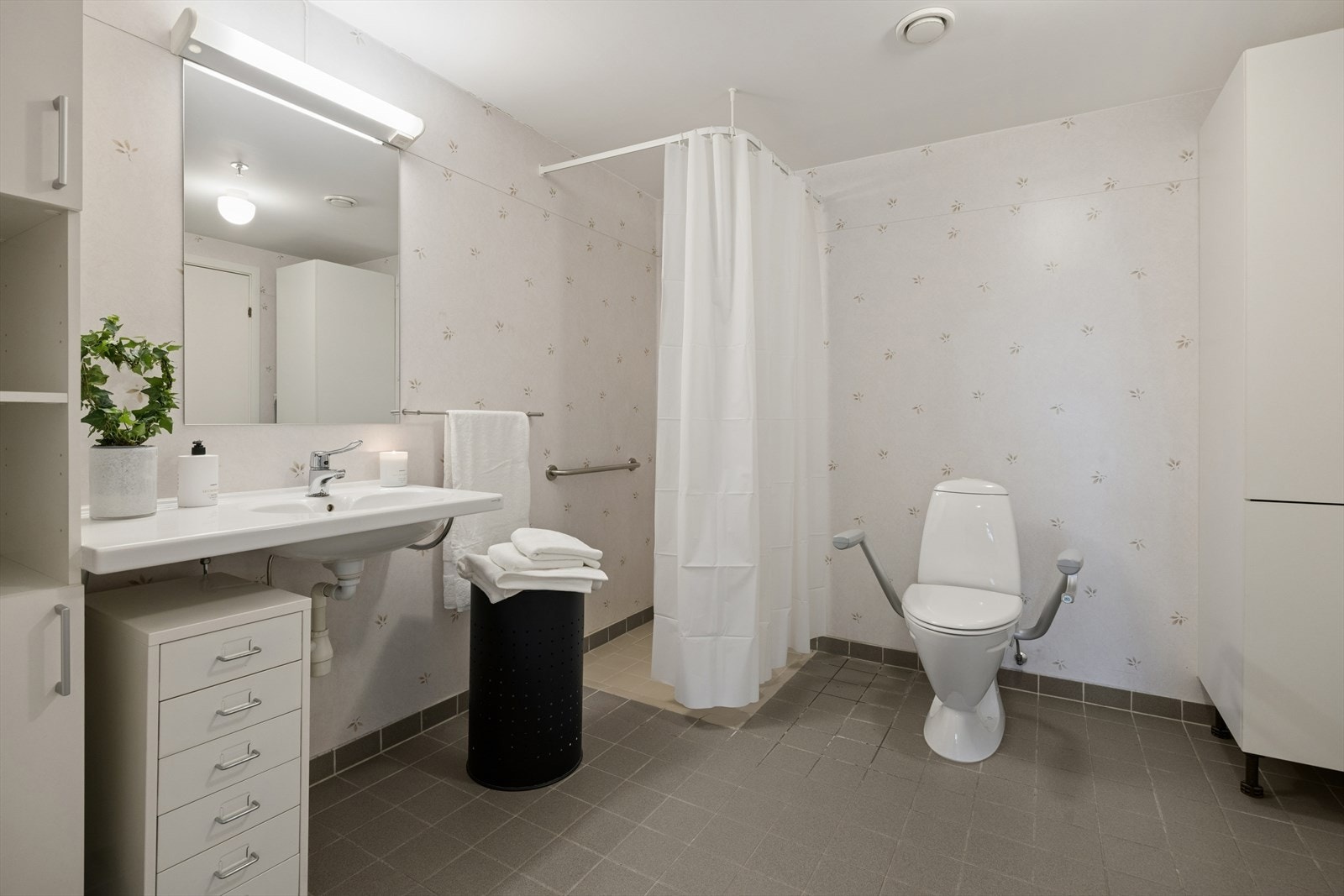 Badet har flislagt gulv og våtromsbelegg på vegger. Rommet er utstyrt med bred servant. Skapinnredning og speil. Opplegg for vaskemaskin. Galleribilde