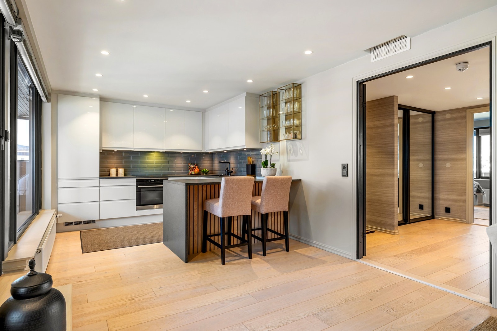 Kjøkkenet har mørk laminert benkeplate og glatte fronter i hvit høyglans, med grå fliser på vegg over benkeskap Galleribilde