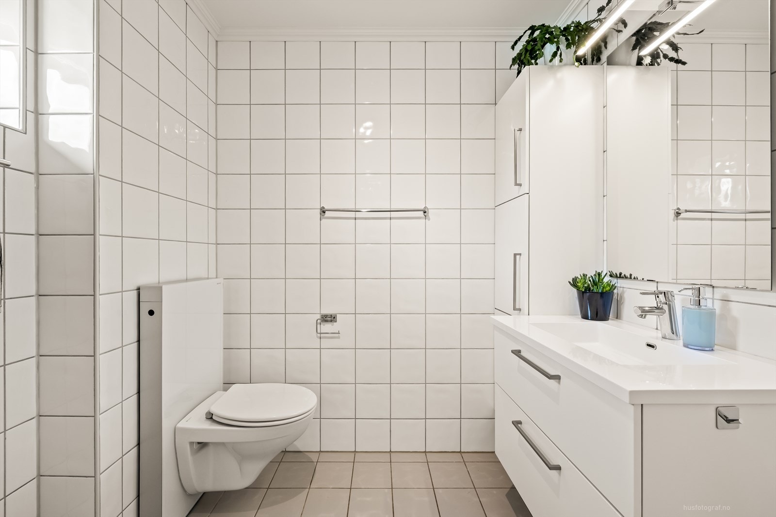 Badet inneholder vegghengt toalett, baderomsinnredning med servant og dusjhjørne med foldbare dusjdører i glass. Galleribilde