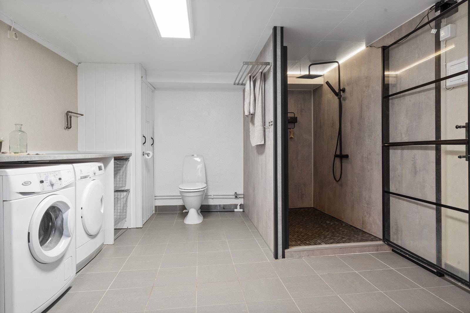 Romslig, flislagt bad med dusjnisje og praktisk opplegg for vaskemaskin og tørketrommel. Galleribilde