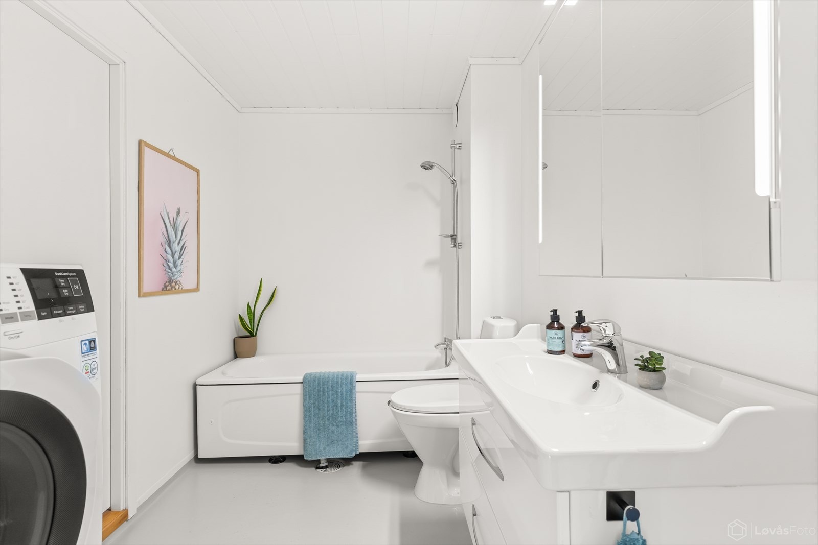Lyst bad med badekar, servant med innredning, toalett og varmekabler i gulv. Opplegg for vaskemaskin. Galleribilde
