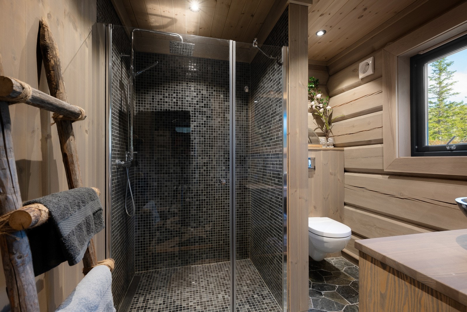 Badet har tømmervegger og flislagt gulv med behagelig gulvvarme. Det er fliser på veggene i dusjsonen. Galleribilde
