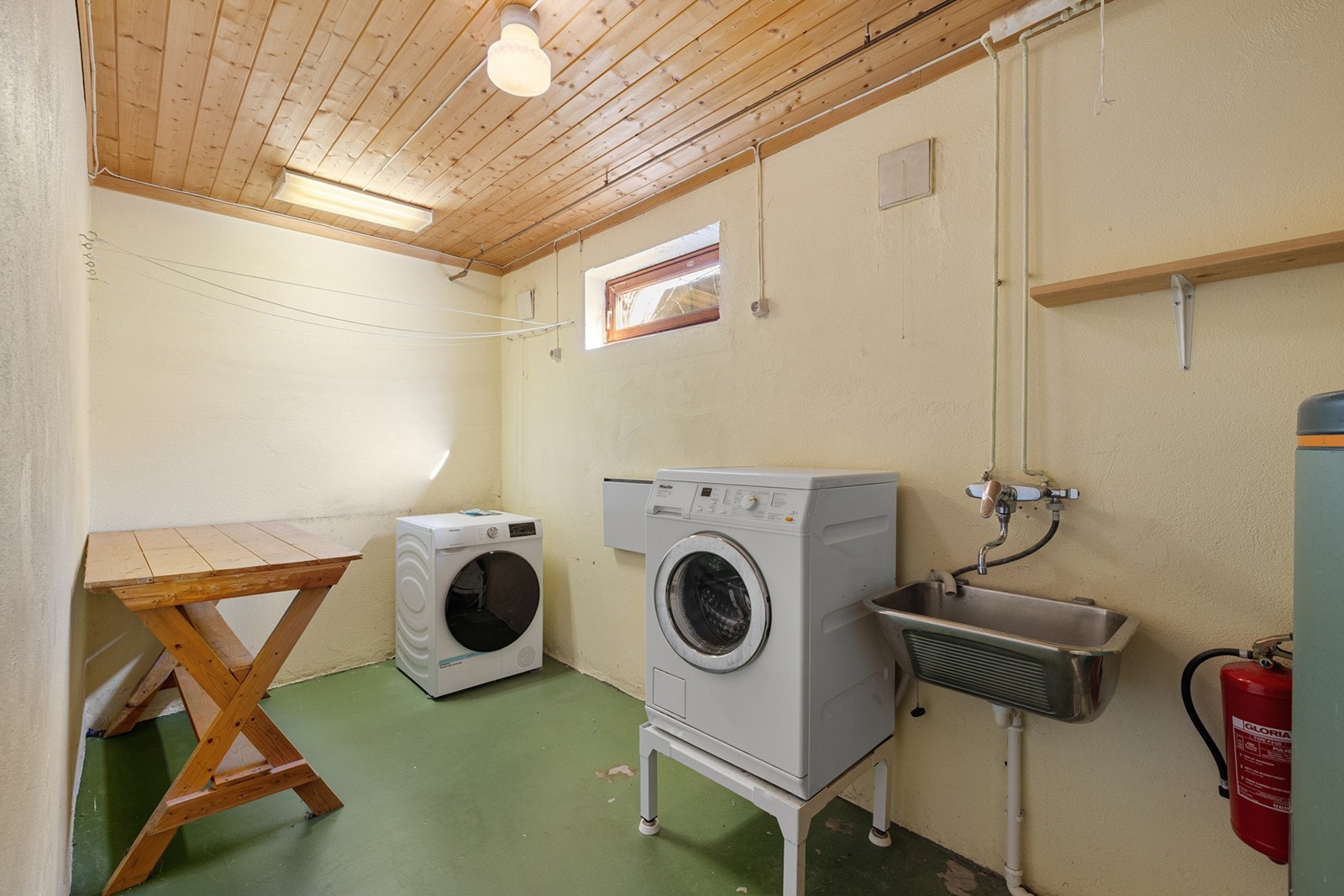 Praktisk vaskerom med sluk, utslagsvask og opplegg for vaskemaskin. Det bemerkes at våtrommet bør oppgraderes for å tilfredsstille dagens krav til bruk og teknisk standard. Galleribilde