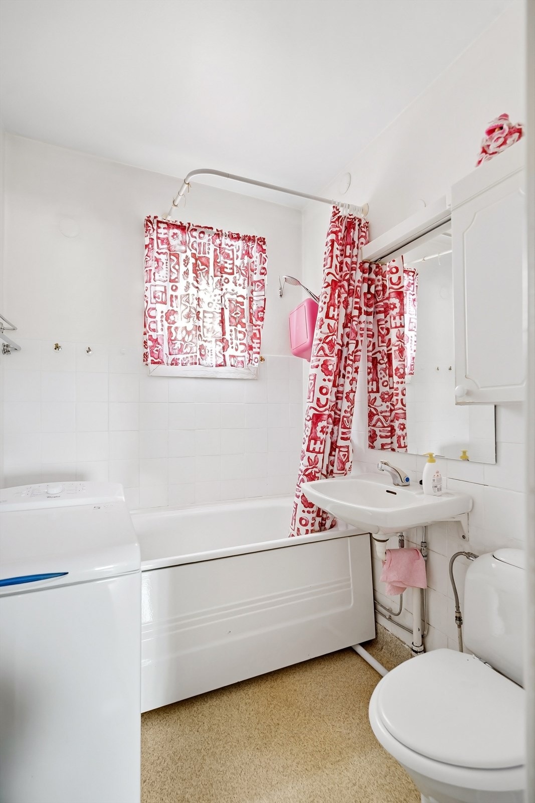 Badet inneholder toalett, badekar, servant, speil med et skap samt opplegg for vaskemaskin Galleribilde