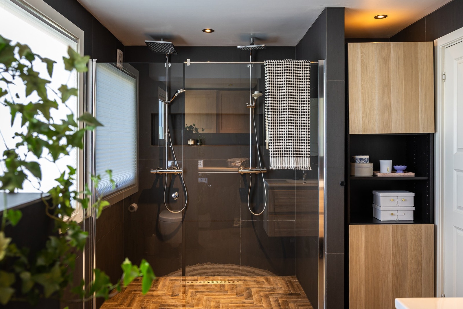 Badet er romslig (ca. 9,8 m²) og fremstår moderne med flislagte vegger og gulv i mørke toner kombinert med varme detaljer i tre. Galleribilde