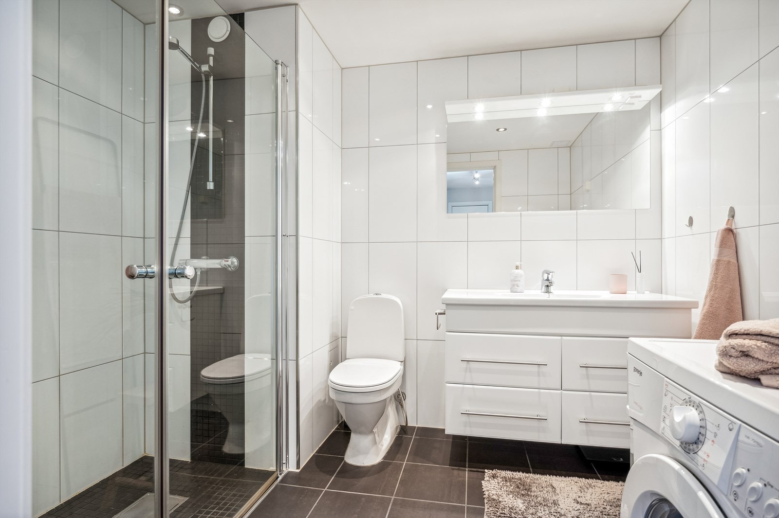 Lyst og pent baderom med flislagte vegger og gulv, samt malte plater med downlights i himlingen. Galleribilde