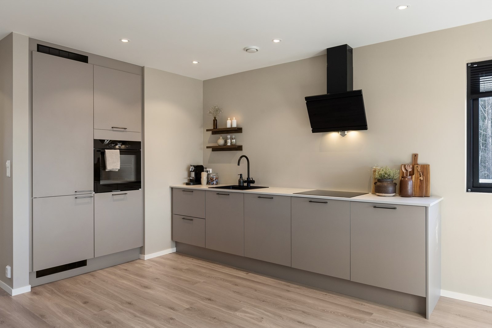 Det moderne kjøkkenet har glatte beige fronter med sorte håndtak som harmonerer med øvrige materialvalg og bidrar til et rolig og stilrent uttrykk. Galleribilde