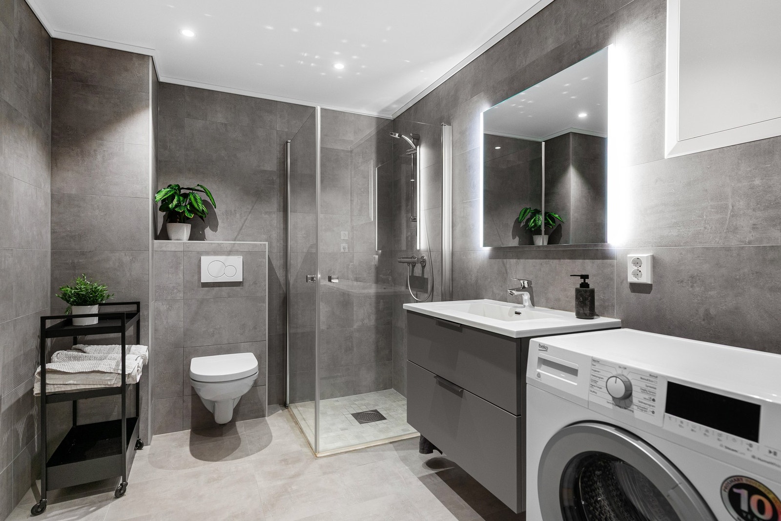 Romslig bad i moderne stil med opplegg for vaskemaskin. Badet er flislagt med gulvvarme. Baderomsinnredning fra HTH. Galleribilde