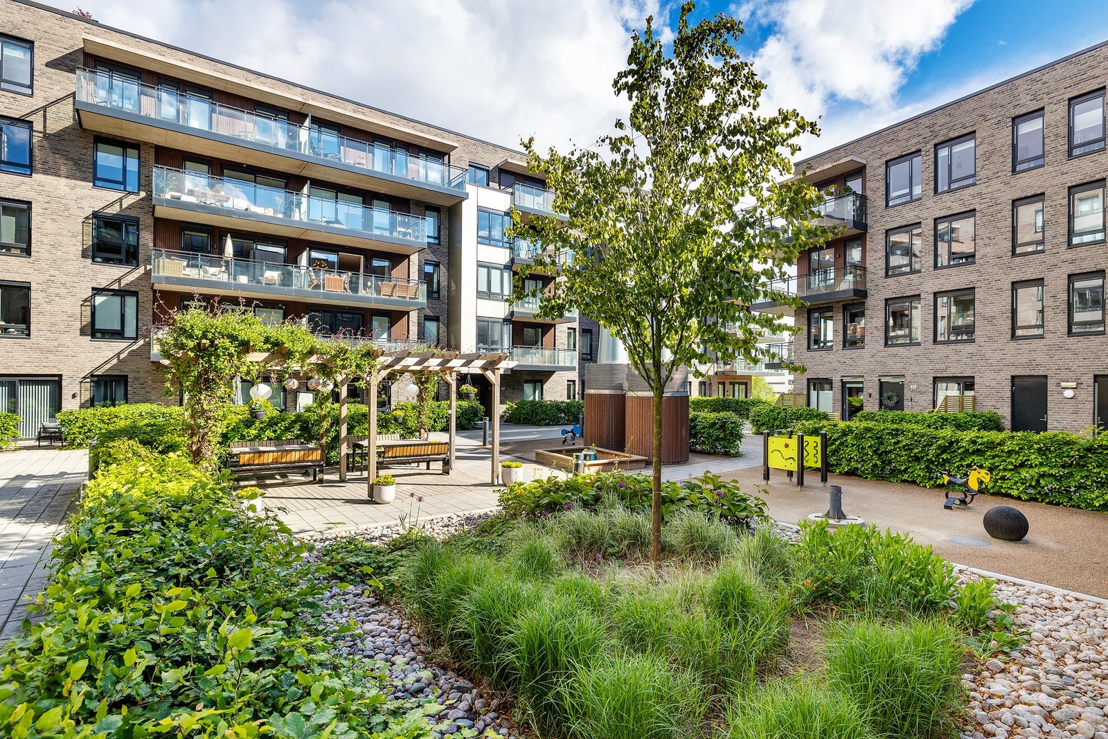 Gårdsplassen i sameiet er pent opparbeidet med sittebenker, pergola og lekeplass for de minste. Galleribilde
