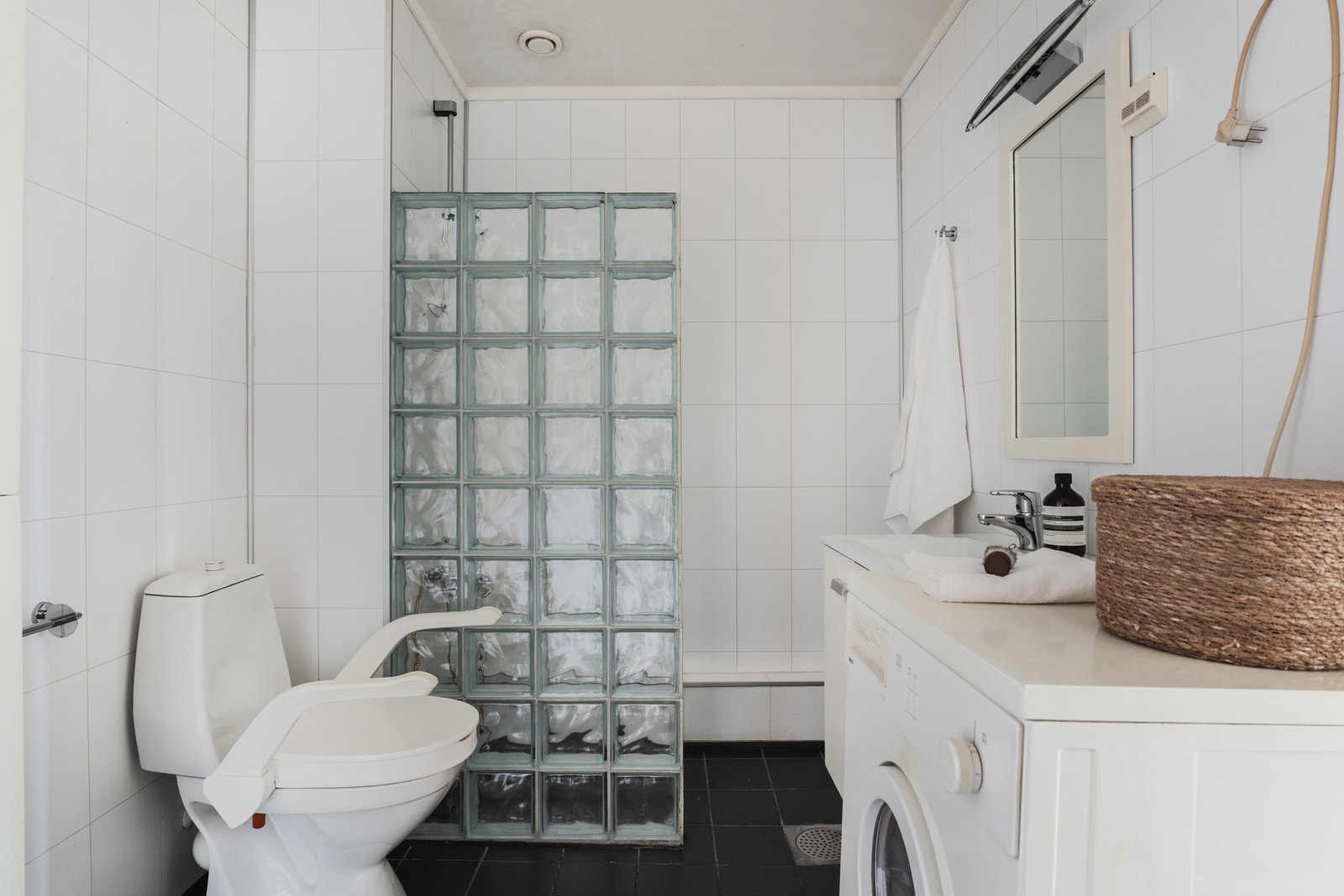 Flislagt bad med praktisk og funksjonell utforming. Badet er innredet med gulvstående toalett, servantskap med nedfelt servant samt dusjløsning adskilt med glassbyggestein. Det er opplegg for vaskemaskin. Galleribilde