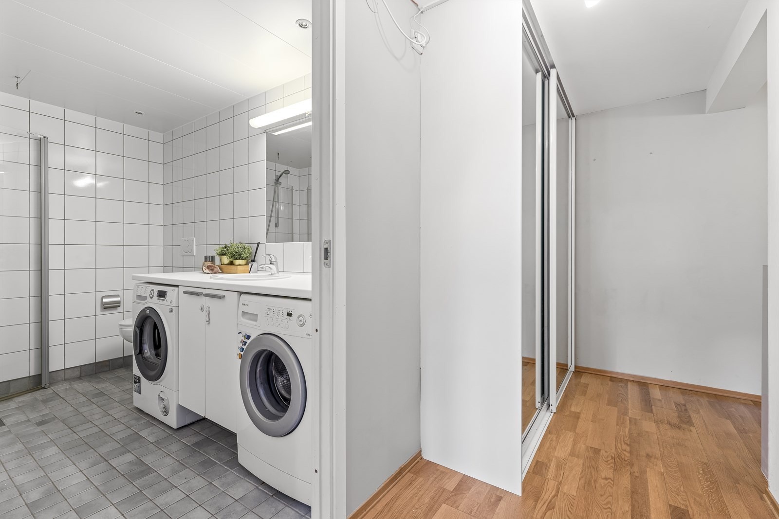 Badet er innredet med nedfelt servant i underskap, veggmontert toalett og dusjhjørne med buede svingdører. Galleribilde