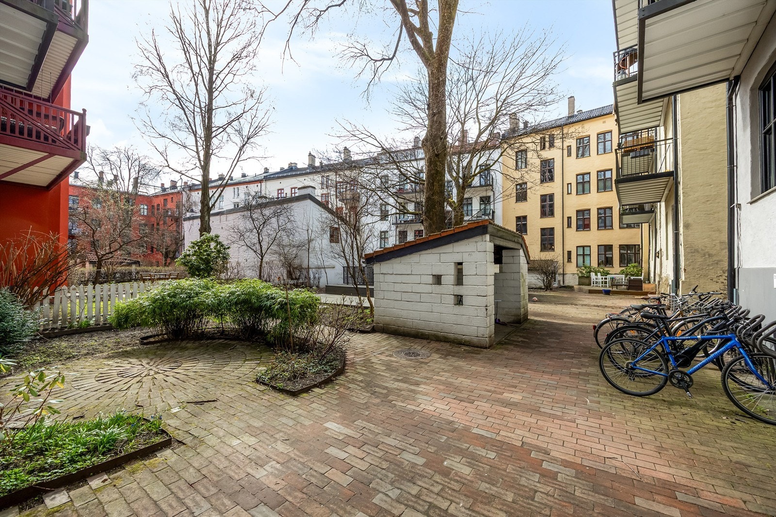 Hyggelig bakgård bestående av diverse beplantning, prydbusker og steinbelagte arealer bestående av gangbaner. Galleribilde