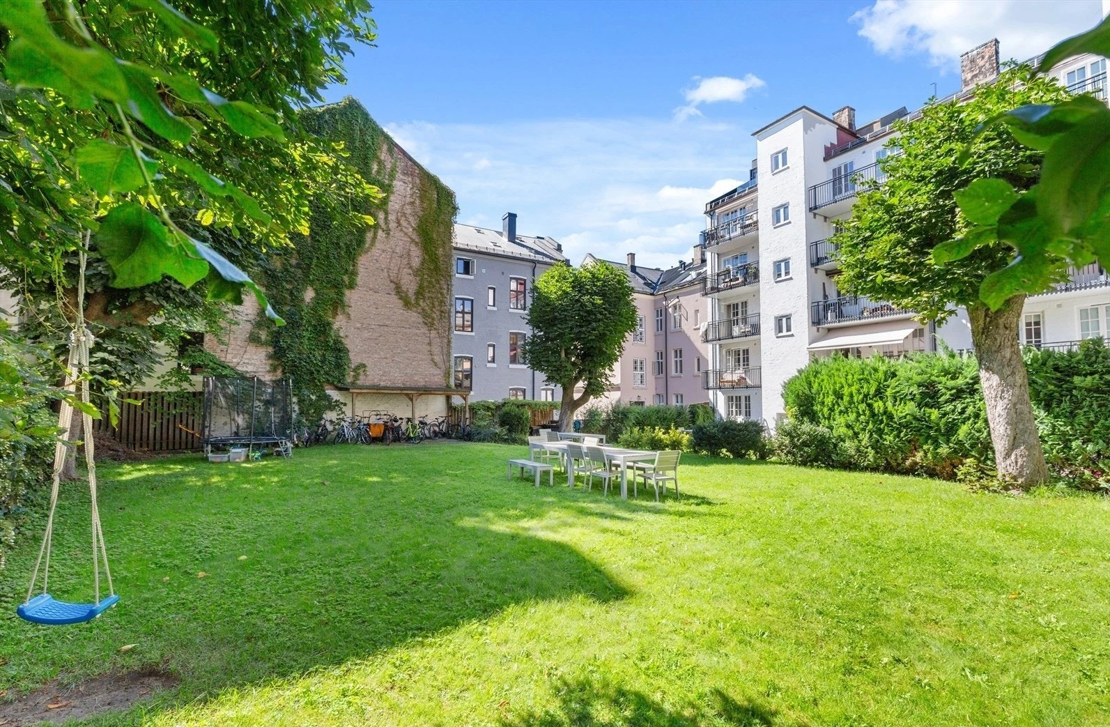 Pent opparbeidet fellesareal med flere sittegrupper, sykkelparkering under tak, plen, beplantning og idyllisk indre bakgård med lange avstander mellom blokkene. Galleribilde