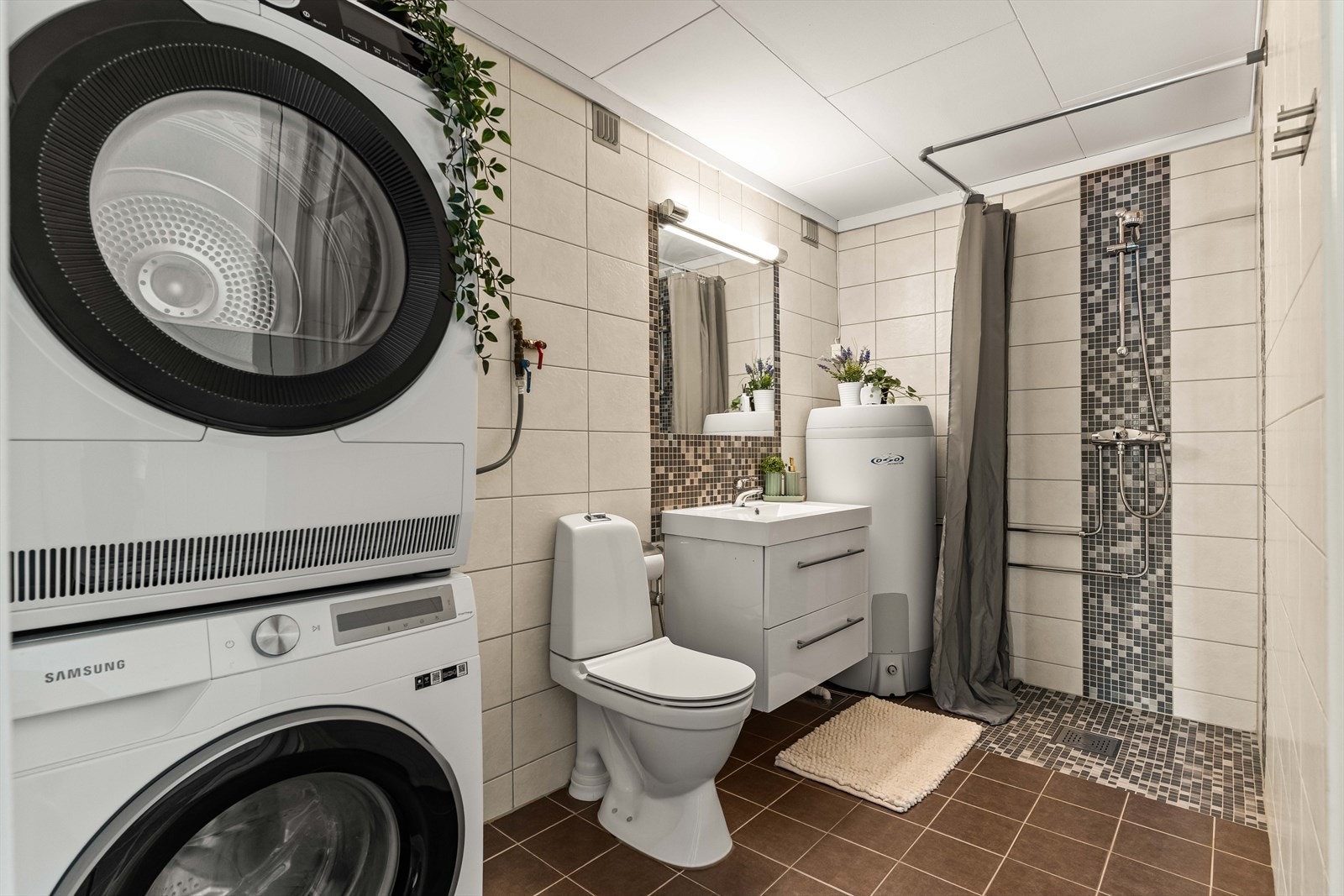 Flislagt baderom fra 2015 med lyse veggfliser og mørke gulvfliser. På badet er det opplegg for vaskemaskin og tørketrommel. Galleribilde