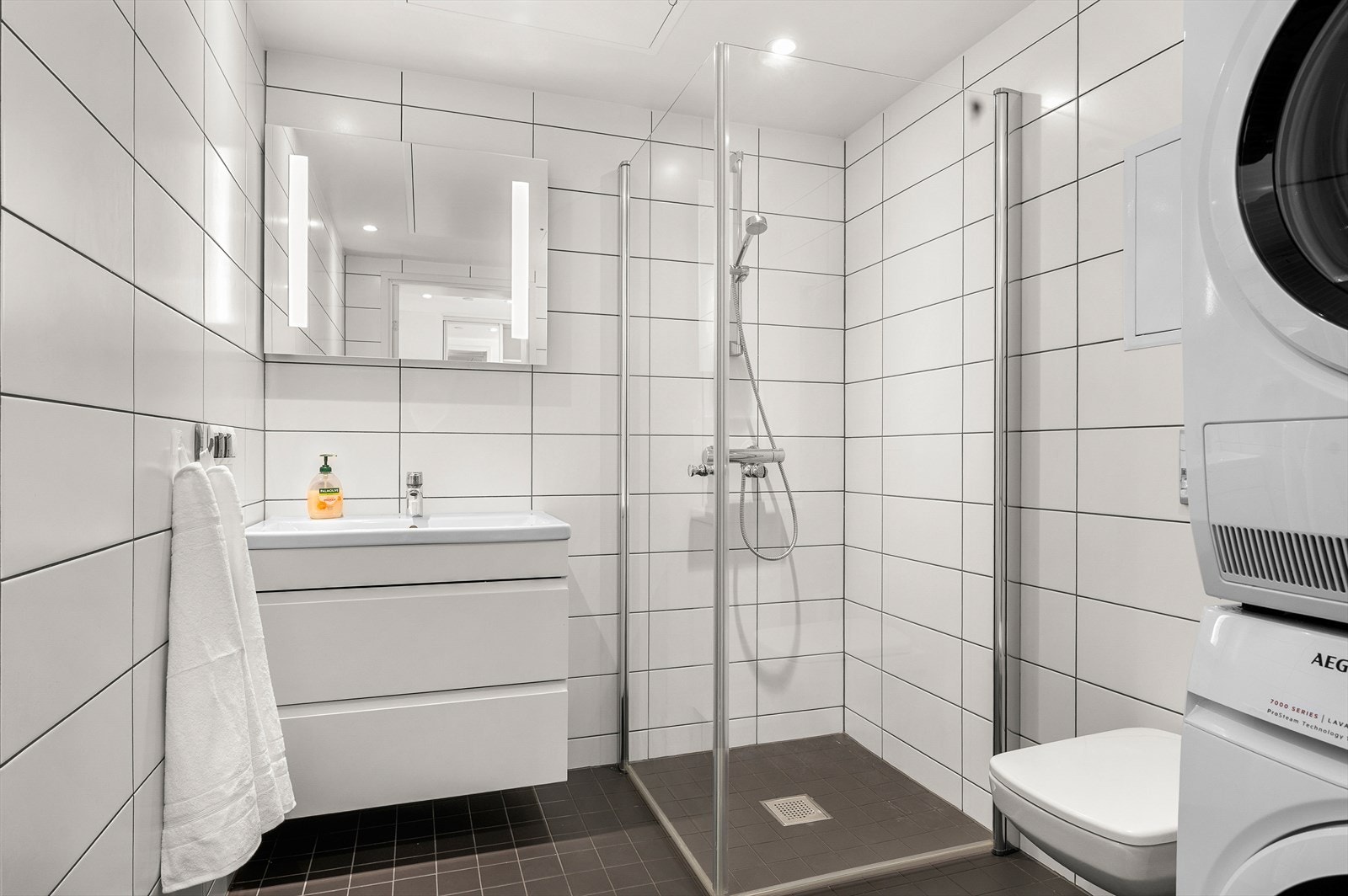 Flislagt bad med behaglig gulvvarme. En rekke kvaliteter som ferdig opplegg for vaskemaskin og tørketrommel, vegghengt toalett, downlights i himling og speil med integrert og servant med skuffer Galleribilde