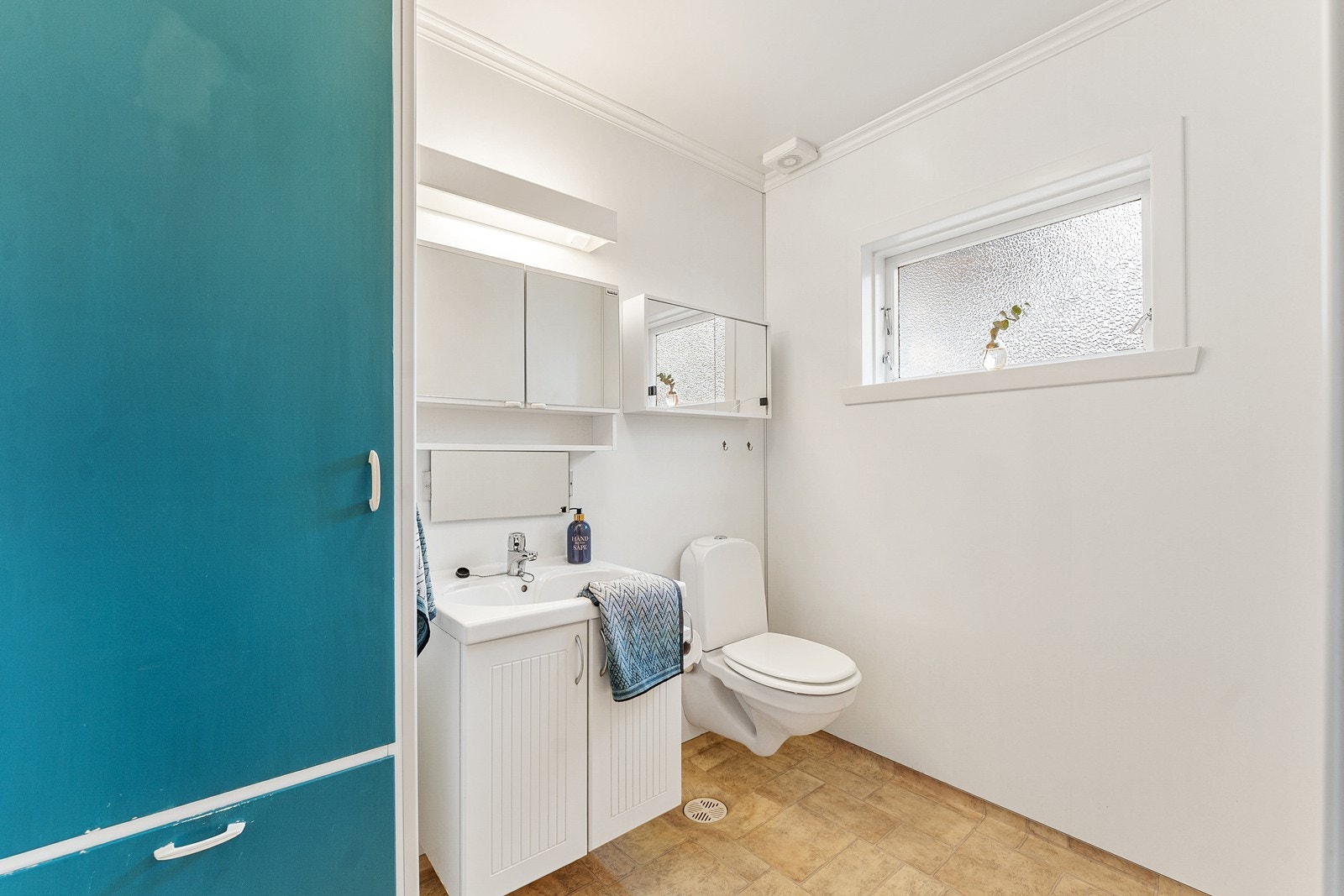 Badet er utstyrt med vegghengt toalett, plassbygget skap samt en enkel baderomsinnredning med servant og ettgreps blandebatteri. Galleribilde