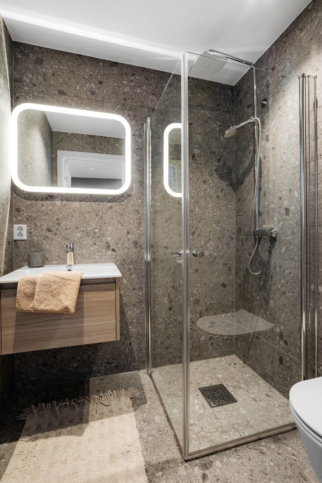 Badet inneholder baderomsinnredning med servant, speil med belysning over servant, dusjhjørne og veggmontert toalett. Galleribilde