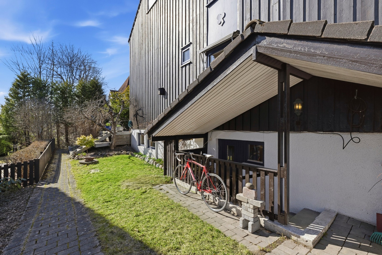 Huset har overbygget inngang til vaskerommet. Plassen under taket er nyttig for sykler eller hageredskaper og er pent belagt med brostein. Kjellertrappen har skiferheller.
På veggen bor fuglene Galleribilde