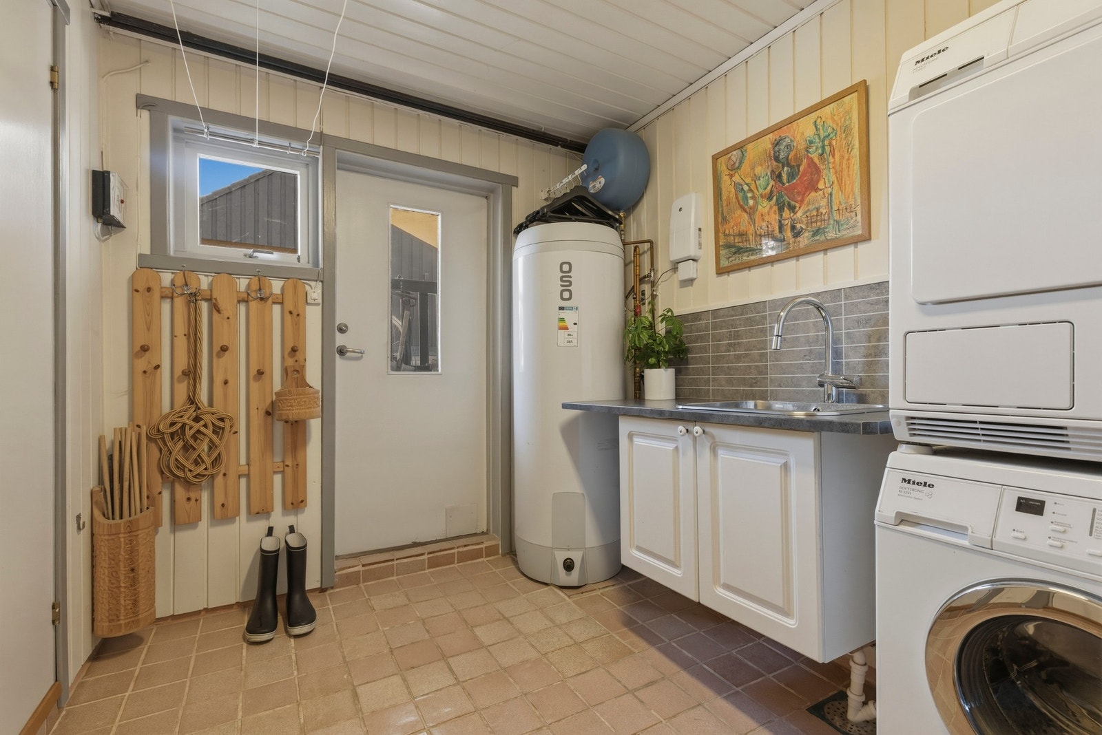 Praktisk vaskerom med direkte utgang til kjellertrapp under tak er praktisk for sølete unger eller hunder eller når man jobber i hagen. Rommet har fliser på gulv med varmekabel. Vaskerommet har sluk, men er ikke vurdert som et våtrom i tilstandsrapporten. Galleribilde