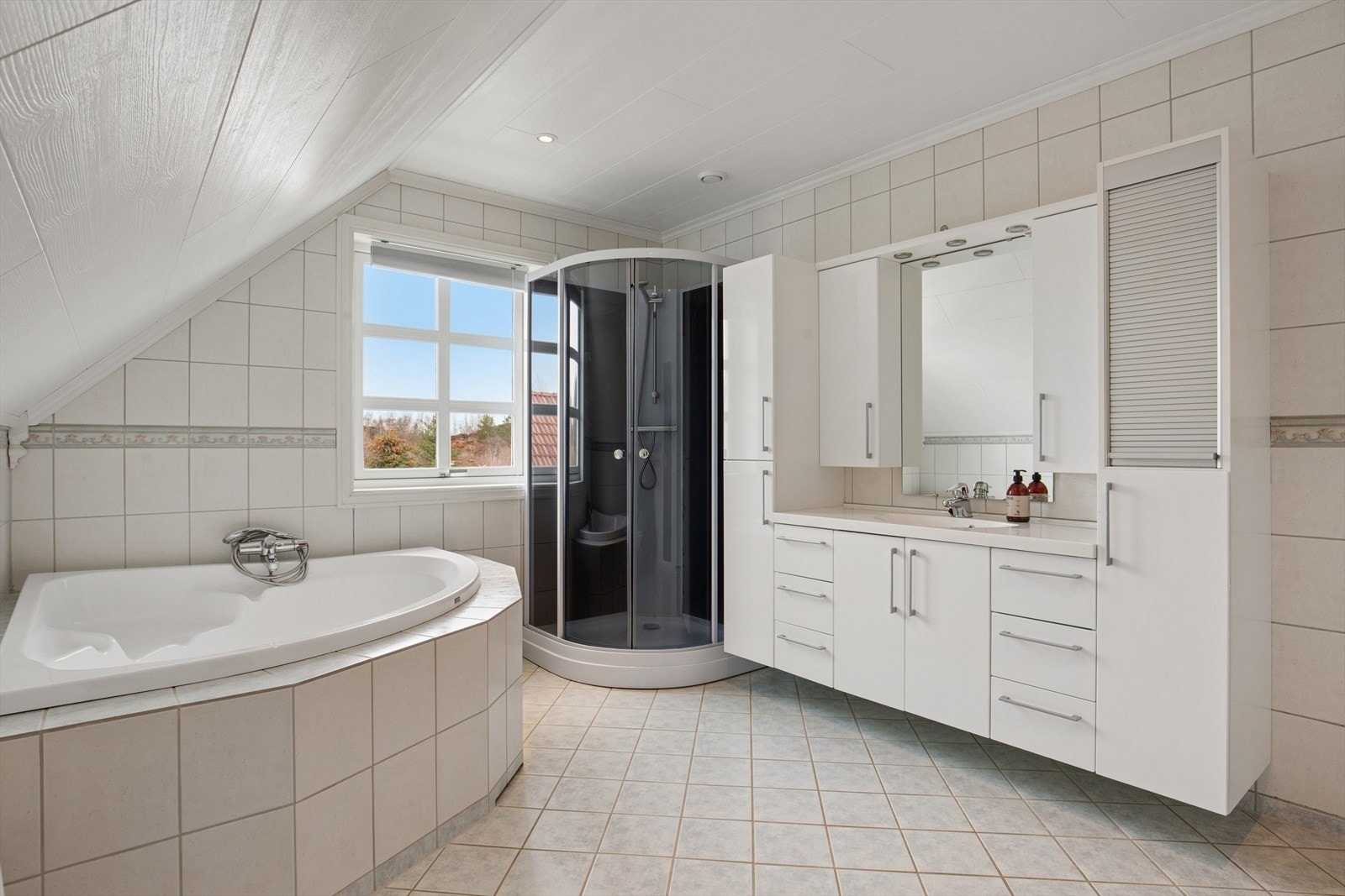 Hovedbadet i loftsetasjen har flislagt gulv med gulvvarme og er innredet med en romslig baderomsinnredning med nedfelt servant samt dusjkabinett. Himlingen er utstyrt med innfelte spotlights som gir behagelig belysning. Galleribilde