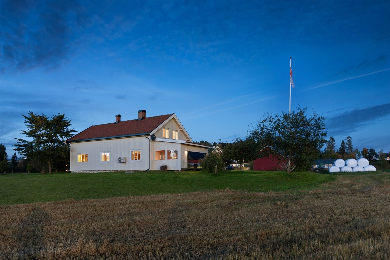 Den store tomten er opparbeidet med plen og beplantning, og grenser mot landbruksarealer. Galleribilde