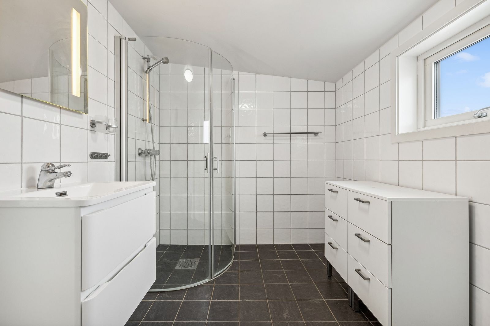 Badet er innredet med vegghengt toalett, vask i seksjon, speil med belysning og dusjhjørne. Galleribilde