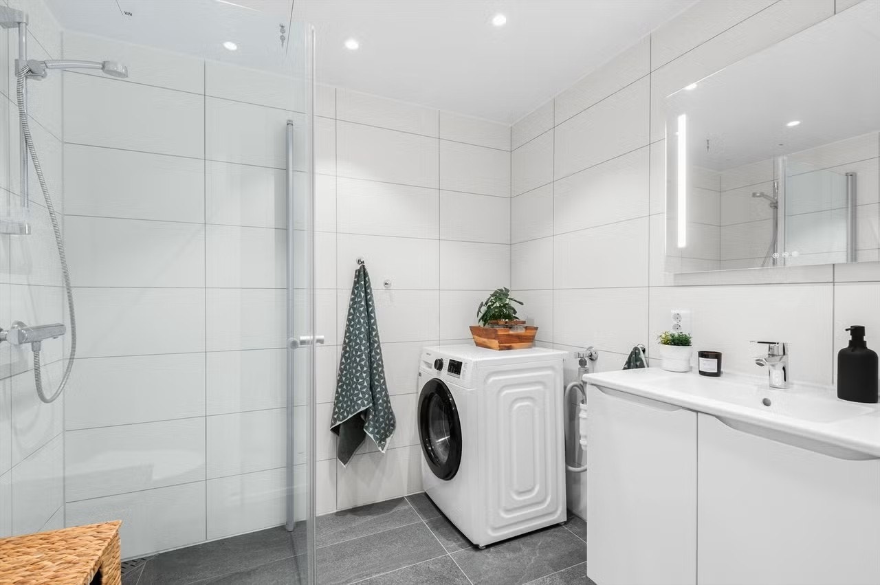 Pent og flislagt bad med innfellbare dusjdører. Det er instarllert vaskemaskin på badet. Galleribilde