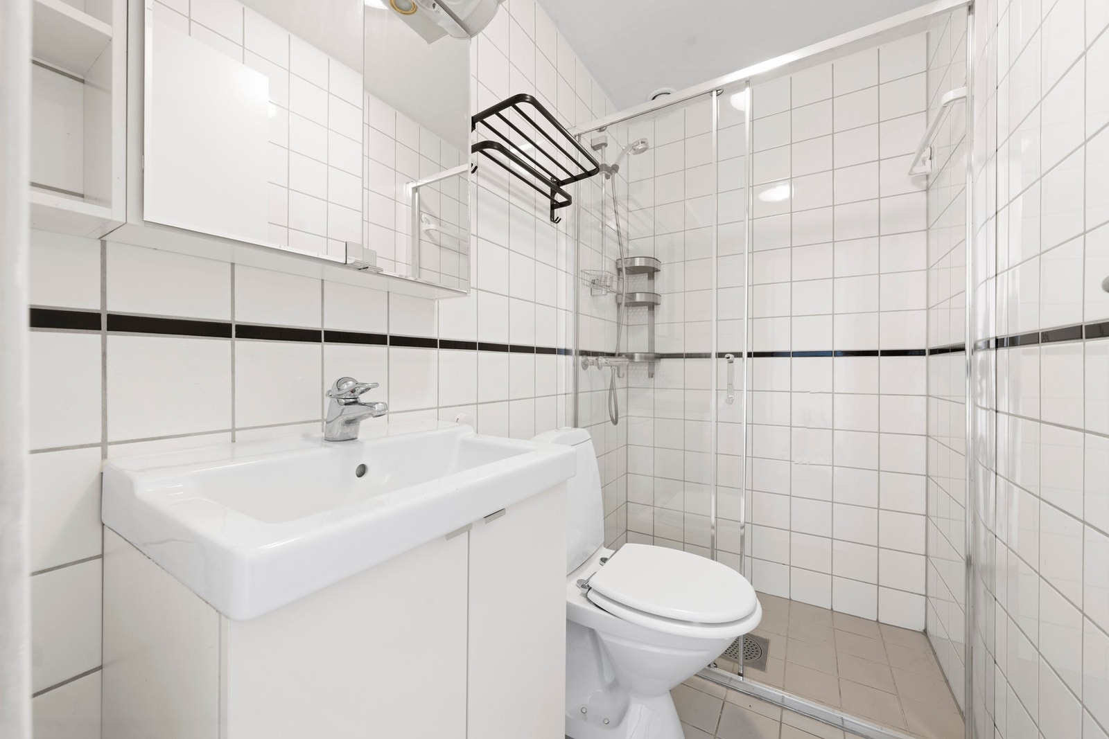 Flislagt bad med varmekabler i gulvet. Badet er innredet med dusjnisje med skyvedør, gulvstående toalett, servant med underskap og speilskap Galleribilde