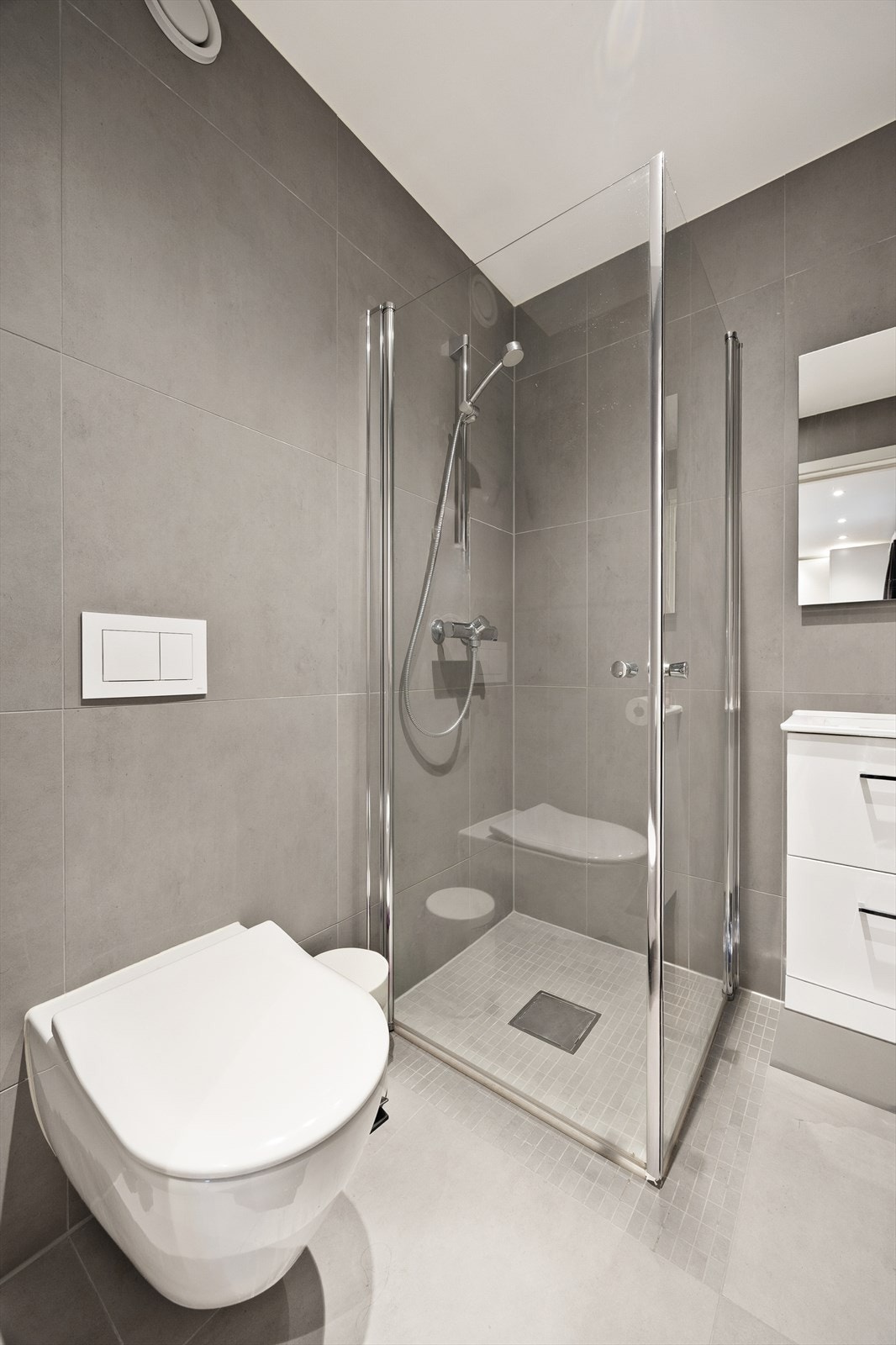 Dette badet er utstyrt med dusjhjørne med innfellbare glassvegger, vegghengt wc og servantinnredning med skuffer Galleribilde