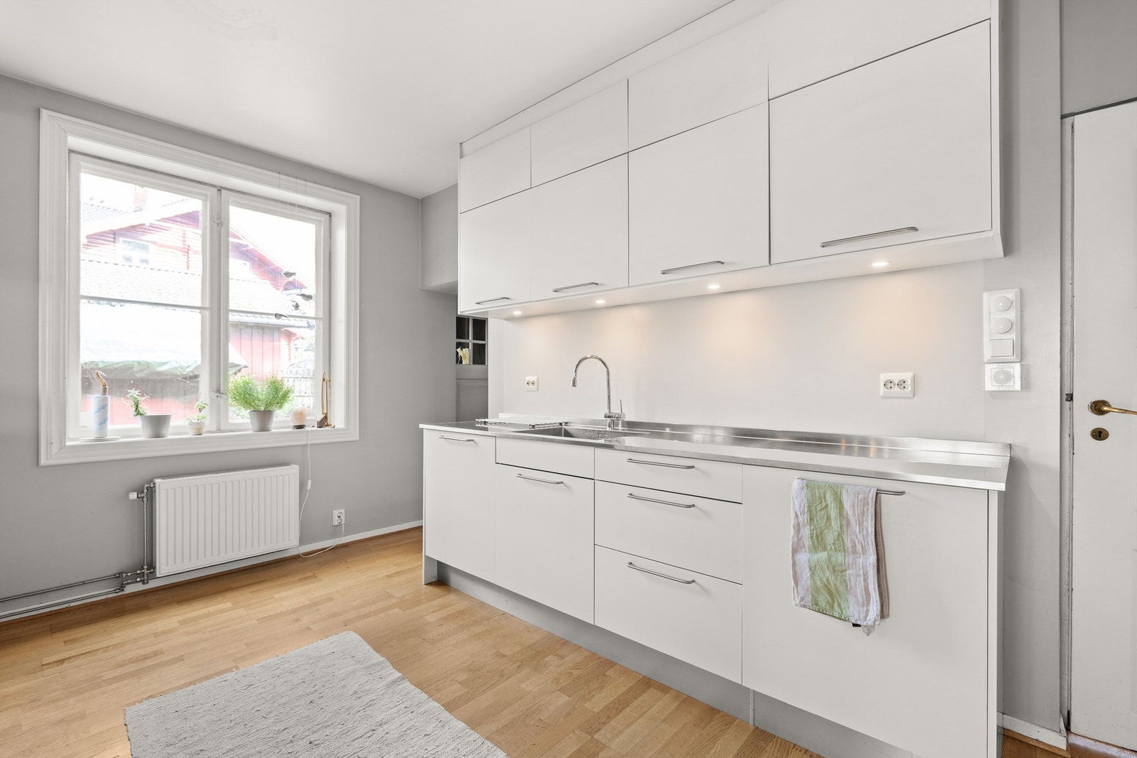 Langs veggen er det en slitesterk benkeplate i rustfritt stål med oppvaskkum og godt med skapplass. Galleribilde