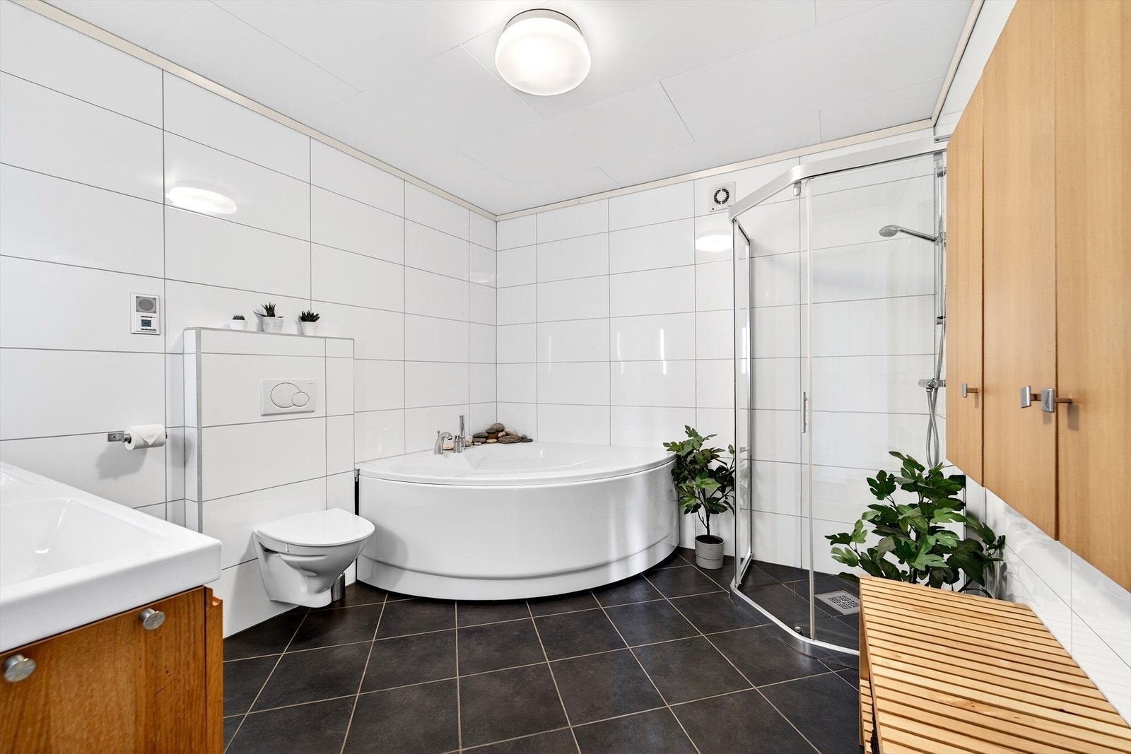 Badet har innredning med dusjhjørne, badekar, vegghengt toalett, nedfelt dobbel servant med skuffeseksjon under og speil med lys. Galleribilde