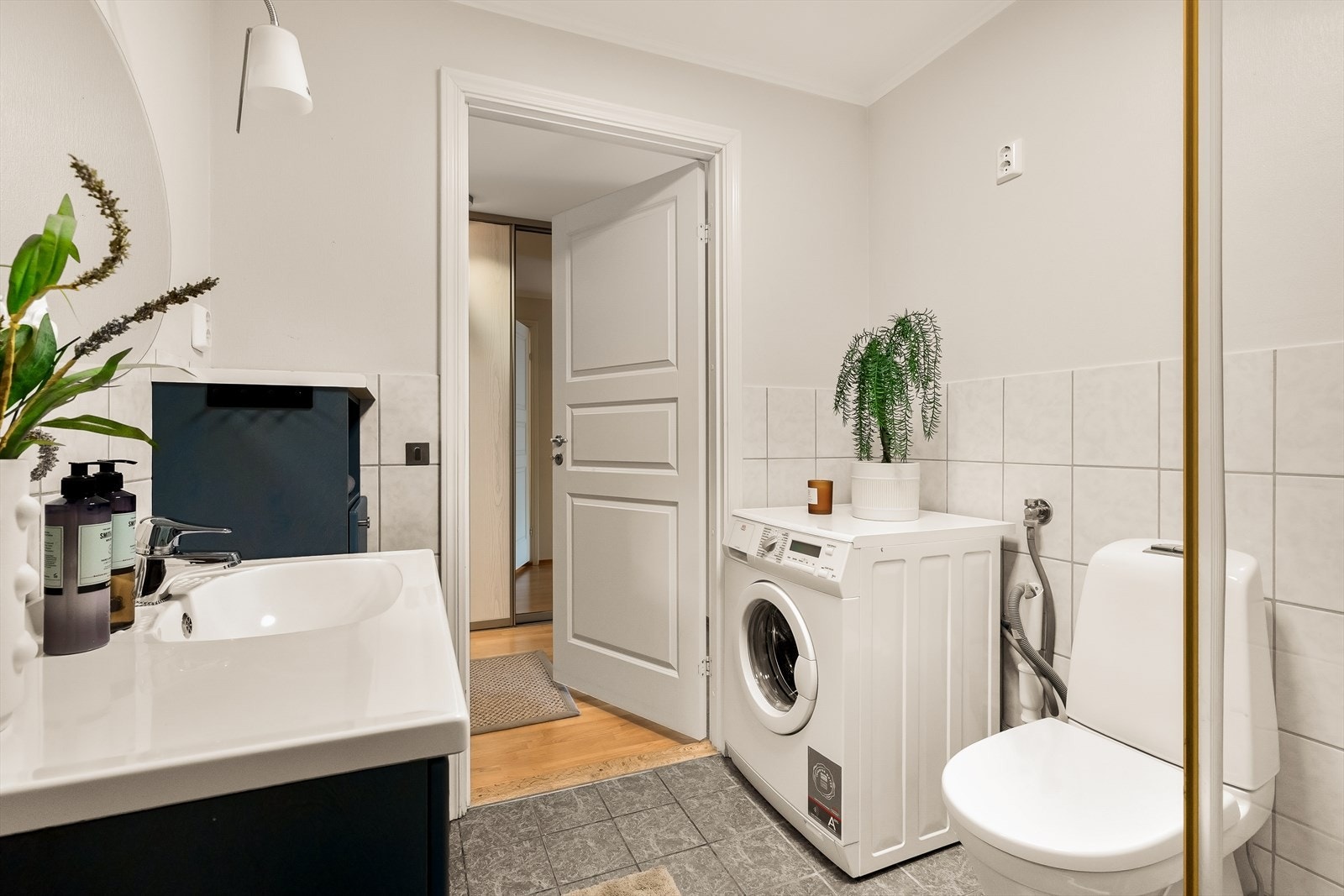 På gulvet er det fliser med varmekabler. Badet er innredet med en pen baderomsinnredning med nedfelt servant, toalett og dusjhjørne, og har i tillegg opplegg for vaskemaskin. Videre er rommet utstyrt med speil og skap som gir gode oppbevaringsmuligheter. Galleribilde
