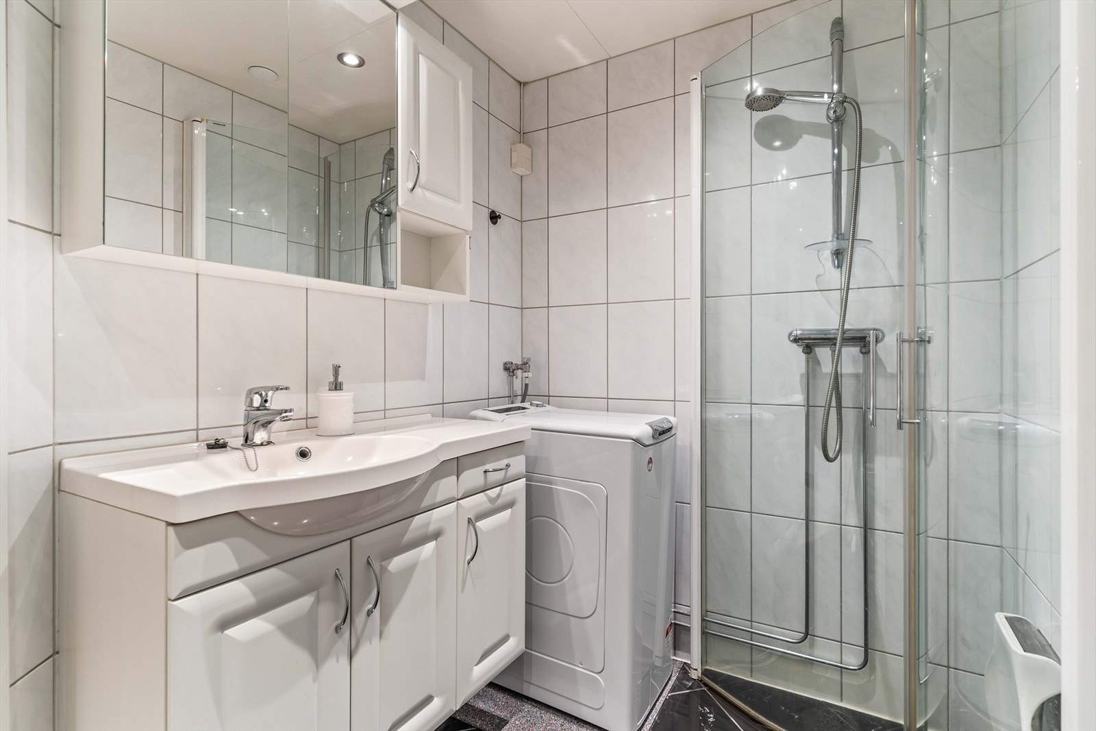 Badet har dusjhjørne med innfellbare glassdører, servantinnredning, speilskap og opplegg for vaskemaskin. Galleribilde