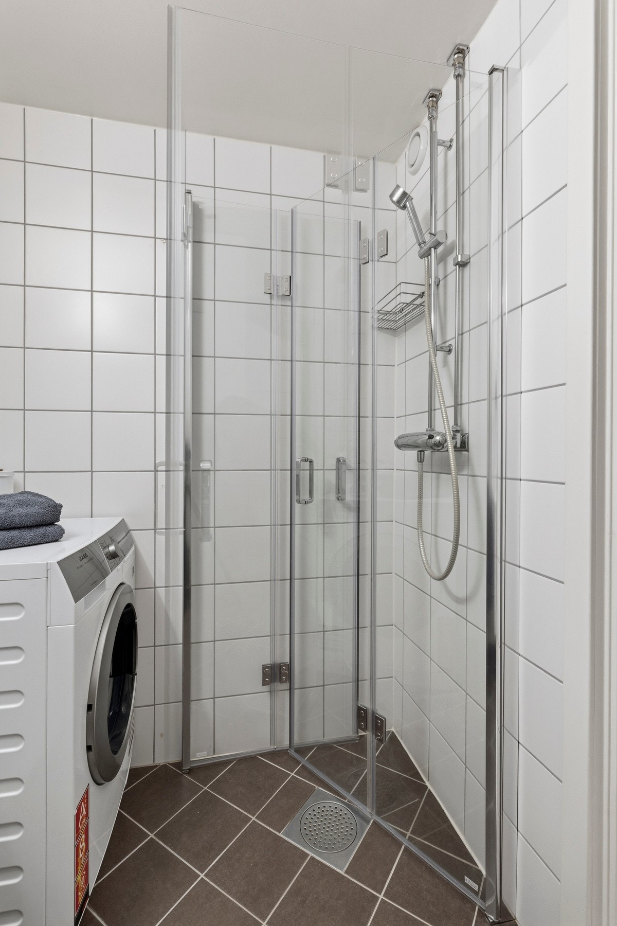 Rommet har en takhøyde på 2,18 meter og er utstyrt med veggmontert toalett, servant med slette fronter, dusjhjørne med to foldbare glassdører og opplegg for vaskemaskin Galleribilde