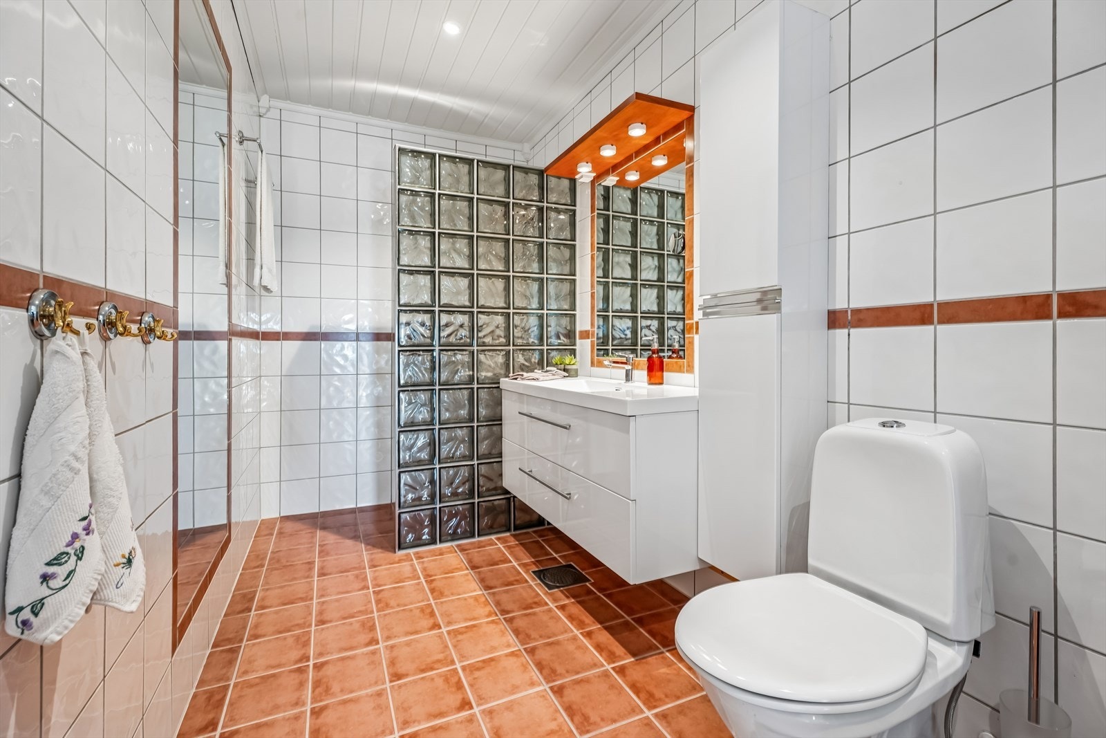 Badet i første etasje har fliser på gulv og vegger, gulvvarme og en praktisk dusjnisje. Galleribilde