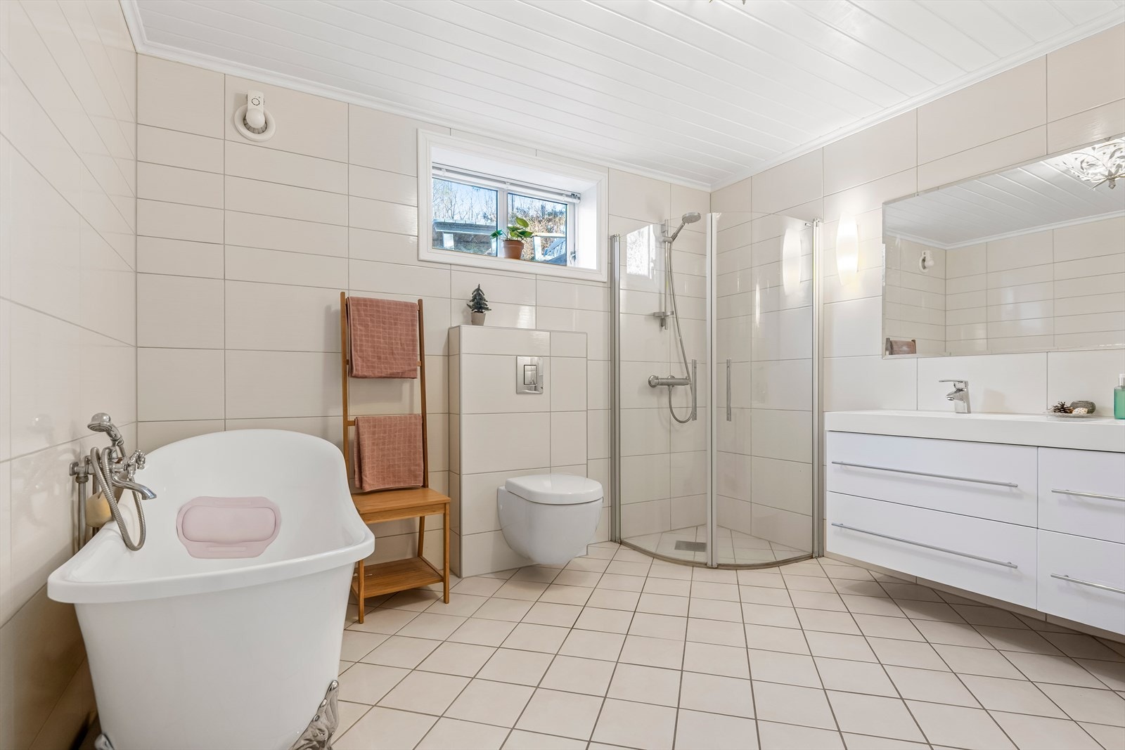 Badet er innredet med doble servanter, vegghengt toalett, dusjhjørne med glassdører og badekar. Galleribilde