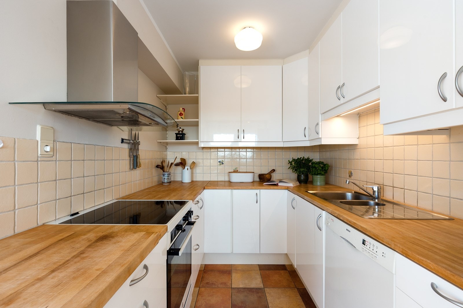 Flis på vegg over heltre benkeplate, med gode arbeidsflater og nedfelt benkebeslag i rustfritt stål. Ventilator med avtrekk ut. Galleribilde