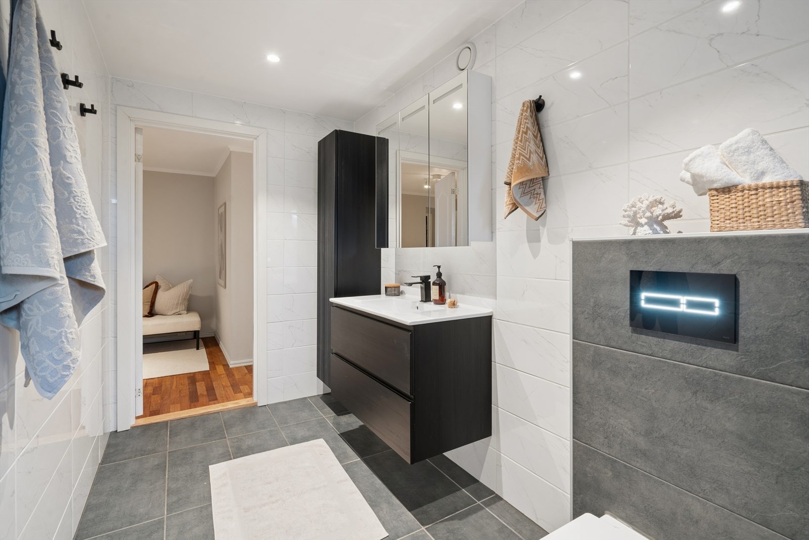 Badet er innredet med veggmontert WC, dusj med dusjvegger samt servant med ettgreps blandebatteri i stilren baderomsinnredning Galleribilde