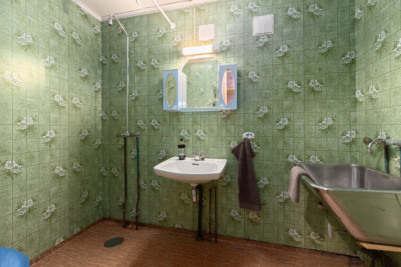 Badet har belegg på gulv og tapet på vegger. Rommet er innredet med skyllekar, enkel servant og innredning med speilskap og lys,
åpen dusj og gulvtoalett. Rommet har naturlig ventilasjon og reflektorovn på vegg. Galleribilde