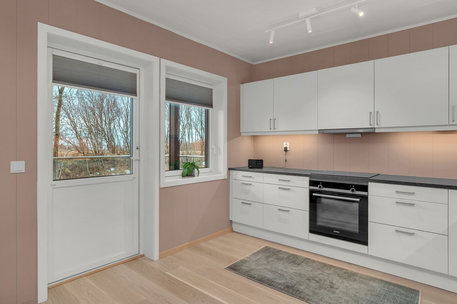 Lyst og moderne kjøkken med integrerte hvitevarer og utgang til en overbygd terrasse. Galleribilde