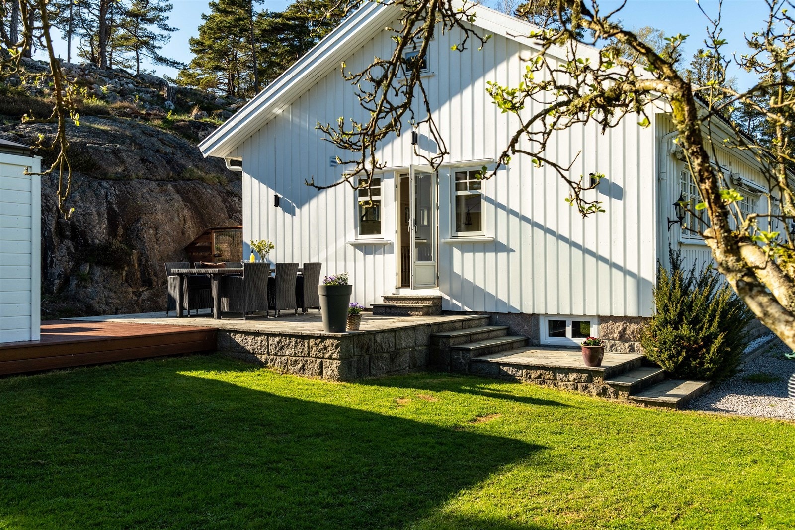 Eneboligen, opprinnelig fra 1958, er et nikk til den klassiske Hvaler-stilen: hvit panelkledning, solide granittmurer og sprossevinduer som fanger dagslyset og gir utsikt mot grønne trær og blå himmel. Galleribilde